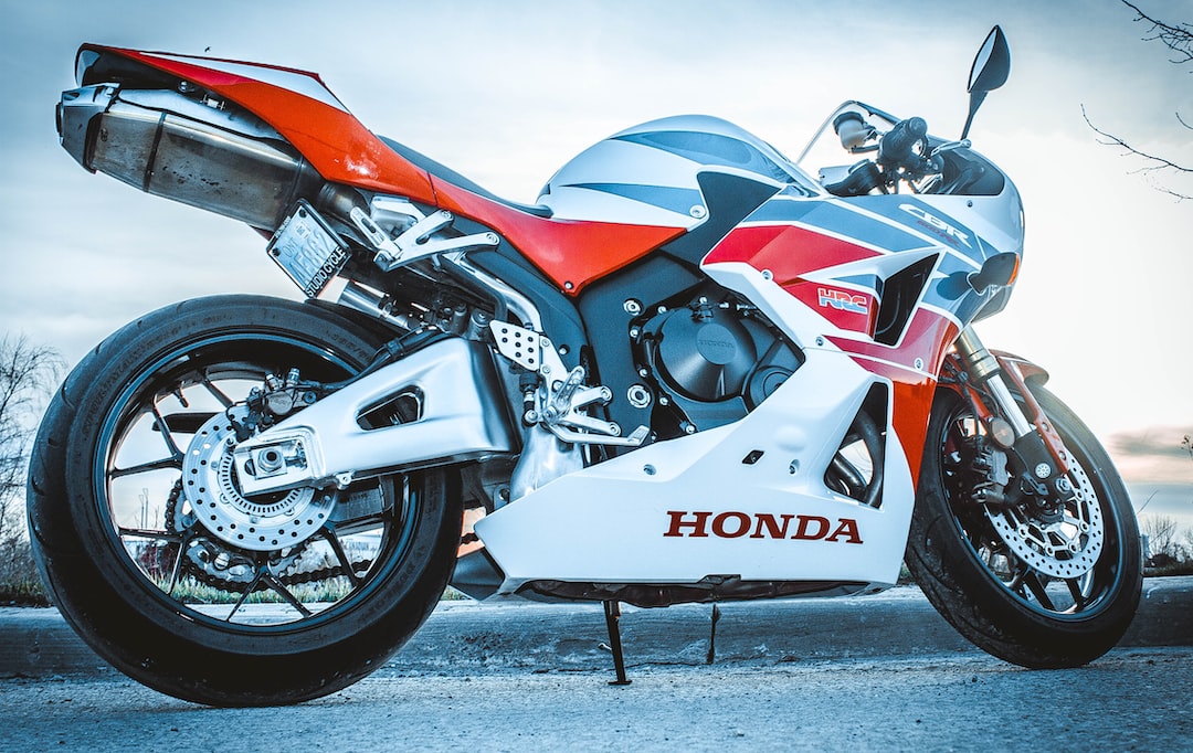 Una motocicleta deportiva Honda roja, blanca y azul destila lujo mientras está aparcada en una superficie pavimentada, vista desde un ángulo trasero bajo.